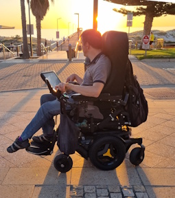 Darryl in his electric wheelchair looking away to the setting sun over the a jetty.
